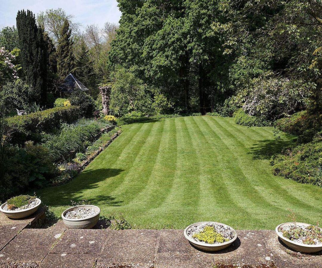 Pas gemaaid gazon met maaistroken, omringd door borders en bomen